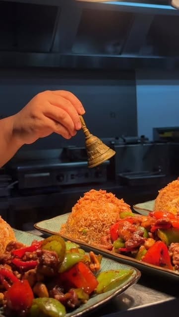 Hand met een belletje boven gebakken rijst en een wokgerecht met paprika